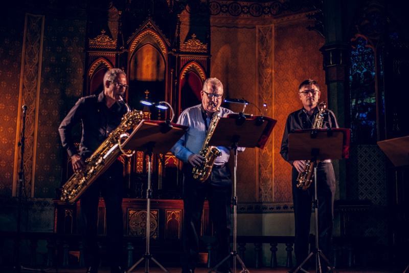 Três saxofonistas diante de um altar dourado