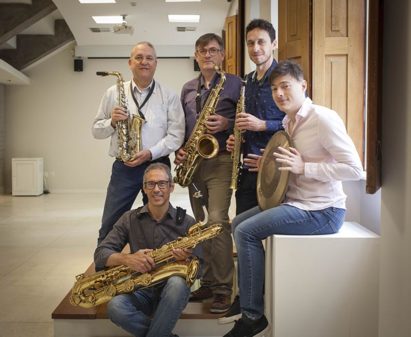 O grupo num salão claro, com saxofones e prato