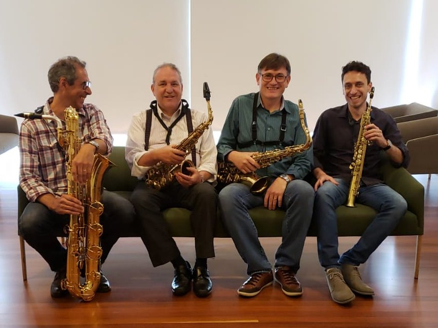 Os quatro saxofonistas do Barlavento sentados num sofá verde, cada um com seu instrumento: barítono, alto, tenor e soprano
